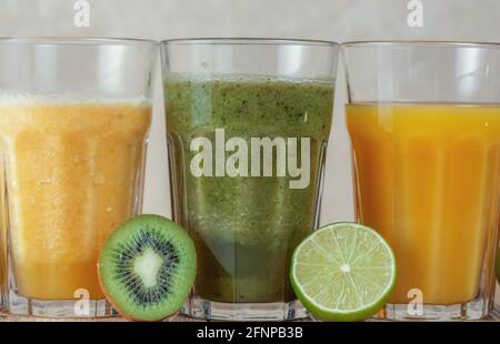 Trois grands verres avec des smoothies aux kiwis et aux épinards dans une rangée entourée de fruits sur une table en bois. Le concept de perte de poids et de nutrition appropriée. Banque D'Images