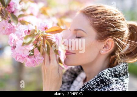 Jeune femme positive qui sent la fleur de cerisier, vue de profil, yeux fermés Banque D'Images