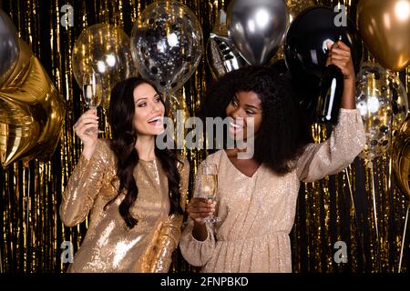 Photo de deux femmes aux cheveux marron glamout contenant une bouteille de champagne les escrocs fêtent l'isolement sur un fond lumineux et lumineux Banque D'Images