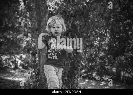 Jeune garçon aux cheveux blonds jouant dans un parc ombragé en été Banque D'Images