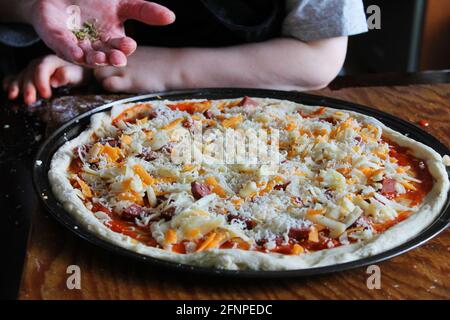 Gros plan sur une pizza maison faite par une femme et un petit enfant. Mains uniquement dans le cadre. Banque D'Images