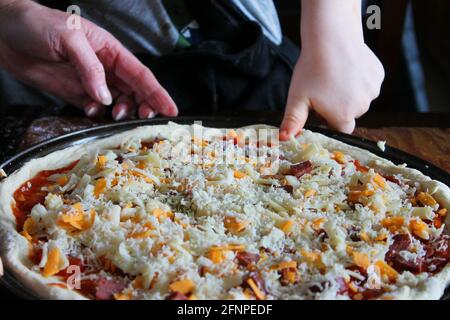 Gros plan sur une pizza maison faite par une femme et un petit enfant. Mains uniquement dans le cadre. Banque D'Images