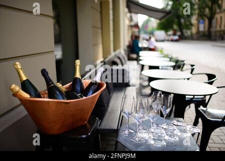 Bouteilles de champagne et de vin mousseux dans un seau à glace en cuivre et des verres à proximité avec une rangée de tables et de chaises vides sur la terrasse du restaurant Banque D'Images