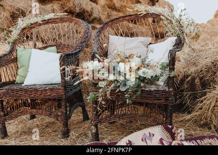 Deux chaises en osier avec coussins et bouquet de fleurs. Chaises en rotin avec des balles de paille en arrière-plan. Style boho Banque D'Images