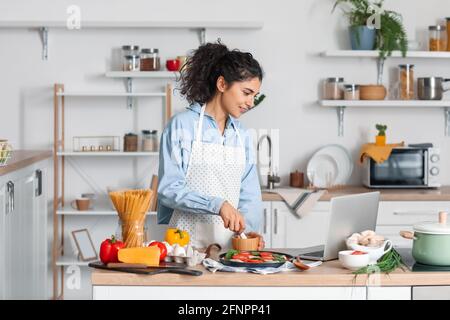 Jeune femme avec mortier et pilon utilisant un ordinateur portable dans la cuisine Banque D'Images