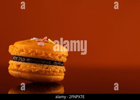 Délicieux macarons orange avec garniture de ganache au chocolat. Délicieux biscuits français isolés. Prise de vue sur fond orange foncé avec réflexions et copie Banque D'Images