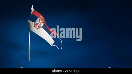 Masque Serbie sur fond bleu foncé. Drapeau de la Serbie peint sur un masque médical sur le poteau. Indicateur d'attaque de virus. Concept de la bannière de la lutte agai Banque D'Images