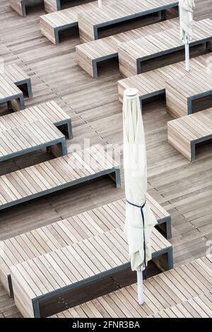 Bancs et rangées de sièges en bois sur une terrasse en bois avec un parasol fermé Banque D'Images
