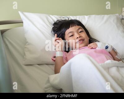 Petite fille asiatique sur le lit d'hôpital regardant la caméra. Banque D'Images