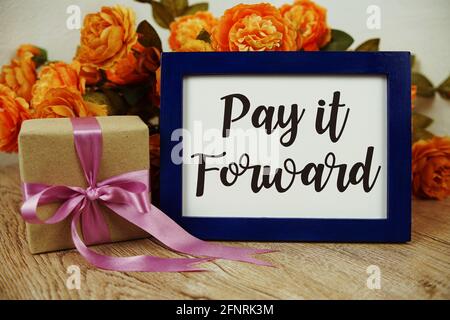 Pay it Forward texte typographique avec boîte-cadeau et fleur sur fond en bois Banque D'Images