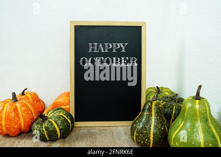 Joyeux octobre texte typographique sur chevalet de bord maquette avec des fleurs artificielles et citrouille sur la décoration intérieure de table en bois Banque D'Images