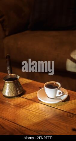 Petite demi-tasse de café grec sur une soucoupe et un briki assis sur une table basse en bois avec fenêtre éclairage Banque D'Images