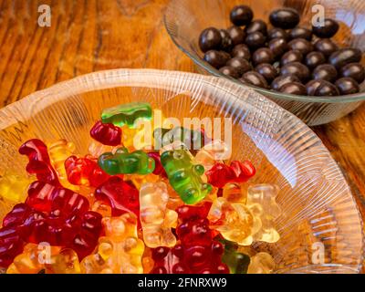 Bols en verre avec des ours en gelée colorés et dans le bol arrière intentionnellement brouillé arachides dans le chocolat, sur un fond en bois Banque D'Images