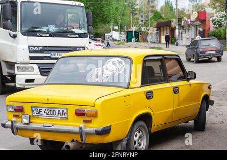 Vue arrière de la berline jaune avec le modèle Joker sur la lunette arrière. La voiture se trouve sur un parking. Un tracteur-remorque blanc passe à proximité Banque D'Images