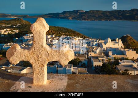 Croix chrétienne et village de Plaka sur l'île de Milos sur rouge Géranium fleurs au coucher du soleil en Grèce Banque D'Images