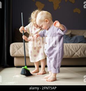 Mignon petits enfants bébé garçon et petite fille dans les vêtements en lin balayer le sol dans la chambre avec le balai, aidant maman avec la maison de corvée à la maison. Le frère de bébé garçon et la sœur aînée passent du temps ensemble Banque D'Images