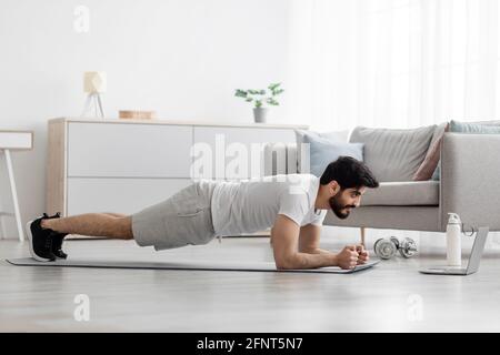 Beau millennium barbu homme arabe faisant des exercices de planche dans la chambre Banque D'Images