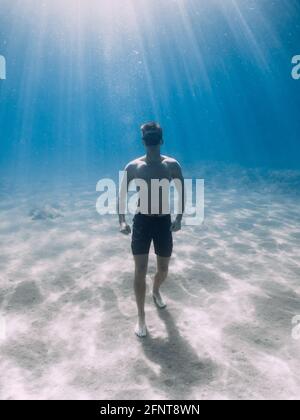 Le frediver sportif reste sur fond sablonneux sous l'eau dans l'océan avec des rayons du soleil. Banque D'Images