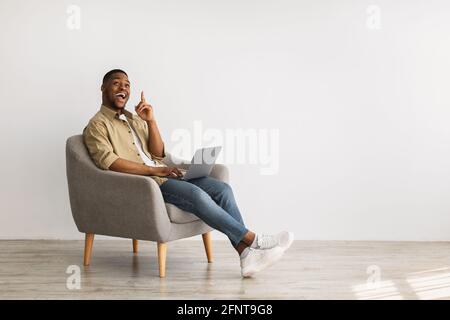 Un homme africain excité avec un ordinateur portable pointant du doigt vers le haut, fond gris Banque D'Images