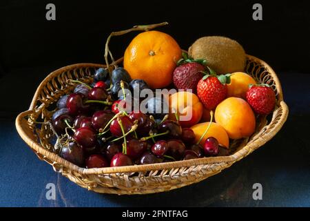 Fruits mûrs dans un panier sur la table avec un reflet. Nourriture sur fond noir Banque D'Images