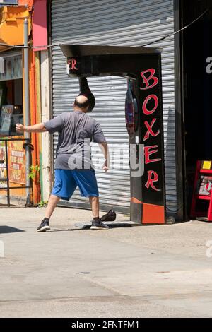 Un homme anonyme d'âge moyen et chauve soulage le stress en prenant une balançoire à un sac de poinçonnage. À Coney Island, Brooklyn, New York. Banque D'Images