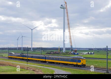 Construction d'éoliennes le long d'un chemin de fer avec un train se précipitant. Concept de transport sur les énergies renouvelables. Banque D'Images