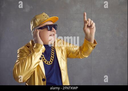 Drôle de DJ senior en blouson doré, casquette de baseball et chaîne de collier mélangeant la musique à la fête disco Banque D'Images