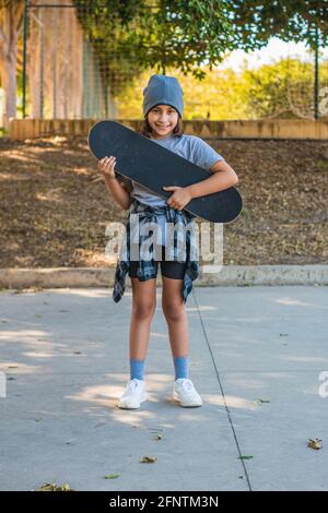 Portrait d'une fille de patineuse caucasienne regardant l'appareil photo, avec son skate très souriant dans un parc de skate Banque D'Images
