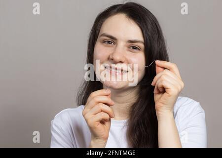 Une brunette brosse ses dents avec du fil dentaire. Hygiène buccale, élimination de la plaque dentaire et prévention de la carie dentaire et de l'inflammation des gencives. Dentisterie Banque D'Images