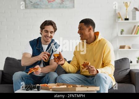 KIEV, UKRAINE - 22 MARS 2021: Des hipsters interraciaux se clinquant avec des bouteilles de bière sur le canapé dans le salon Banque D'Images
