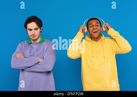 joyeux jeune afro-américain dans des écouteurs avec un ami isolé sur bleu Banque D'Images