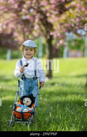 Mode enfant tout-petit, manger de la crème glacée et pousser les enfants poussette avec poupée tricotée dans lui dans le parc Banque D'Images