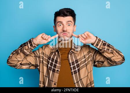 Photo de jeune beau funky drôle choqué homme retenir souffle pointez le doigt sur les joues isolées sur fond bleu Banque D'Images