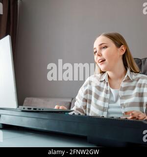 Femme apprend de la musique chantant des voix jouant du piano en ligne à l'aide d'un ordinateur portable à l'intérieur de la maison. Adolescente chante chanson jouer piano synthétiseur pendant la vidéo Banque D'Images