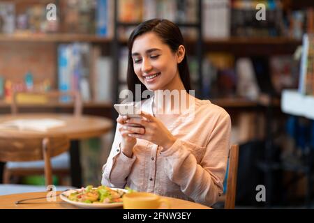 Jeune femme arabe prenant une photo de repas, assise au café et partageant son repas sur un compte de médias sociaux. Banque D'Images