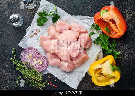 Morceaux crus ingrédients de viande de poulet sur bois, épices, herbes et légumes sur fond gris foncé. Ingrédients crus pour le goulash ou le shish keb Banque D'Images