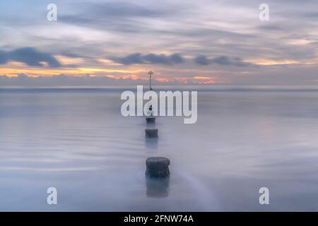 Gronnes en ligne lors d'une journée tranquille au coucher du soleil sur West Wittering Beach, West Sussex Banque D'Images