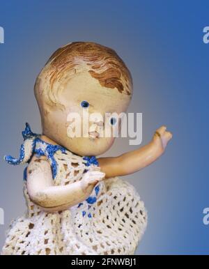 Poupée ancienne craquelée et usée en bleu et blanc robe en crochet sur fond bleu Banque D'Images