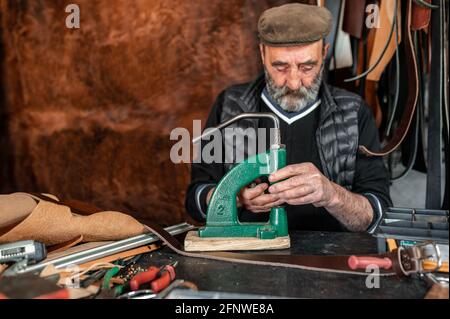 Un artisan expérimenté qui fait des trous dans le cuir avec un perforateur. Arrière-plan en cuir poilu. Banque D'Images