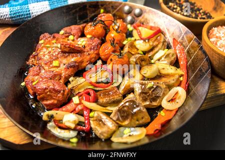 Viande, cou de porc en marinade et sur une poêle en acier. Cou de porc avec pommes de terre cuites au four et légumes avec piment. Banque D'Images