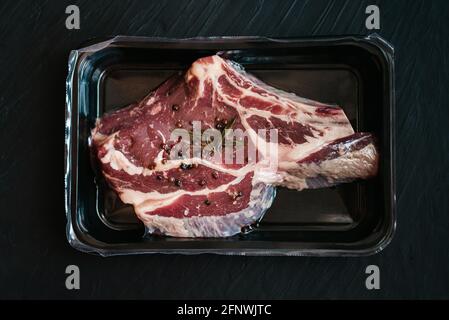 Steak de bœuf cru et épices sous vide sur fond sombre. Vue de dessus. Emballage hermétique. Viande emballée sous vide Banque D'Images