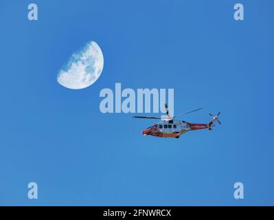 Hélicoptère de garde-côtes volant survolant un ciel bleu vif avec demi-lune, Écosse, Royaume-Uni Banque D'Images