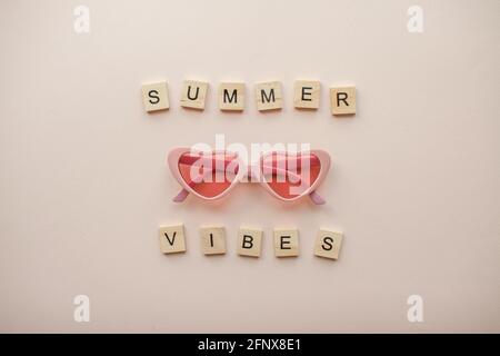 Mise en page. Verres roses sous forme de coeurs sur fond rose clair. Inscription de blocs de bois Summer vibes Banque D'Images