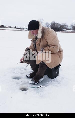 Un pêcheur sur la pêche d'hiver dans des vêtements chauds et des bottes en feutre. Banque D'Images