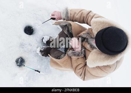 Un pêcheur sur la pêche d'hiver dans des vêtements chauds et des bottes en feutre. Banque D'Images