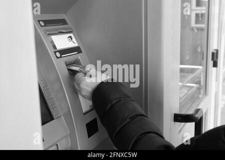 La main d'un homme insère une carte de crédit dans un distributeur automatique de billets. Image en noir et blanc. Banque D'Images