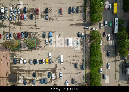 Vue aérienne en haut de la rue animée avec circulation de voitures en mouvement et grand parking avec beaucoup de véhicules garés. Banque D'Images