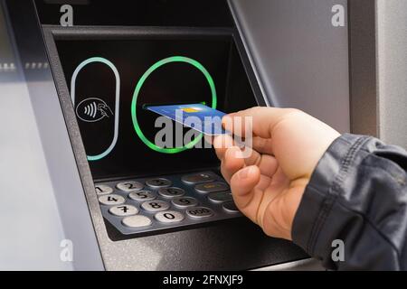 La main de personne caucasienne insère une carte de crédit dans un distributeur automatique de billets. Recevoir de l'argent d'un guichet automatique pendant la journée dans une rue. Retrait d'espèces à l'extérieur. Banque D'Images