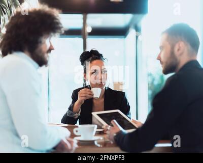 Un groupe de professionnels en pause-café utilisent des ordinateurs portables, des tablettes et des smartphones tout en discutant de nouveaux projets d'entreprise. Banque D'Images