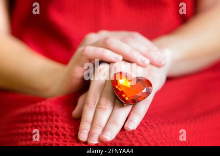 Femme assise en rouge portant un énorme anneau en pierre de faux bijou en forme de coeur avec ses mains sur les tours. Gros plan, mise au point sélective. Banque D'Images